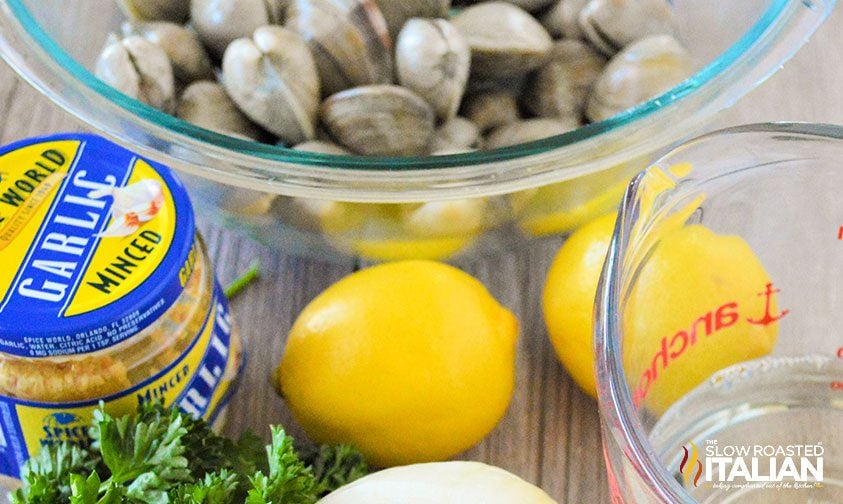 bowl of steamer clams with lemons, wine, and jar of minced garlic