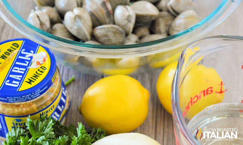 bowl of steamer clams with lemons, wine, and jar of minced garlic