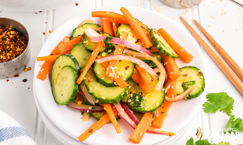 carrot and cucumber salad on a stack of plates with chopsticks and red pepper flakes