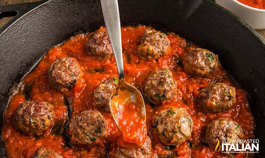 spooning marinara sauce over keto meatballs