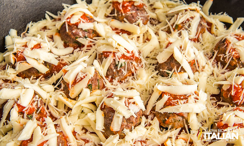 adding shredded cheese on top of cooked meatball casserole in cast iron skillet