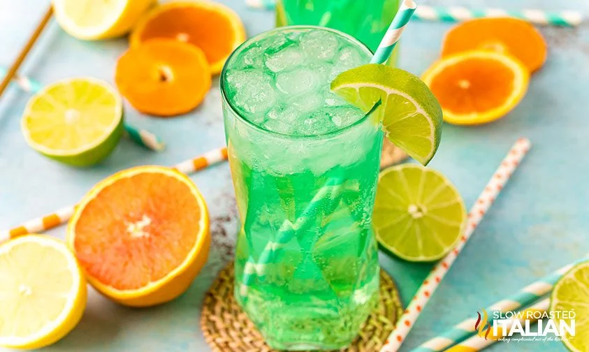 glass of Mountain Dew Baja Blast soda with lime garnish surrounded by citrus fruit