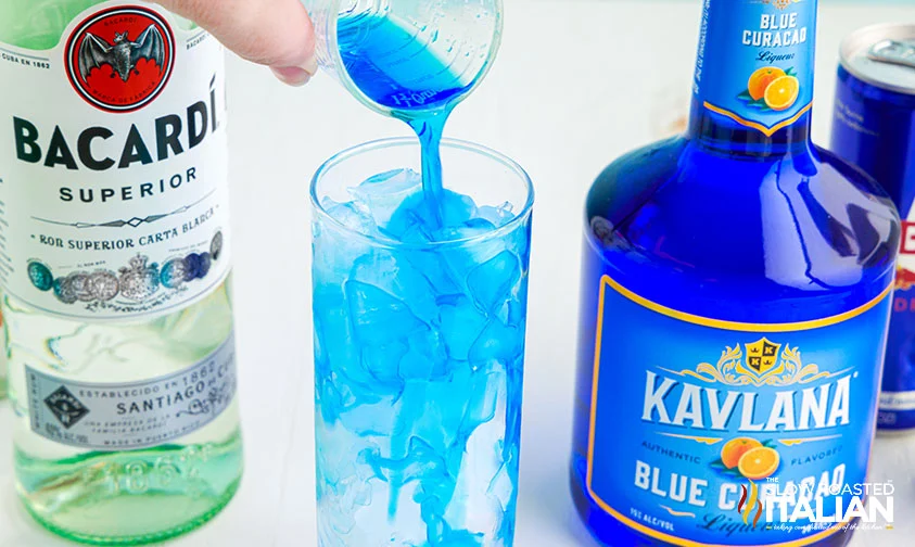 pouring blue curacao into tall glass with ice