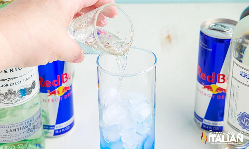 pouring clear liquor into glass with blue curacao for Irish trashcan