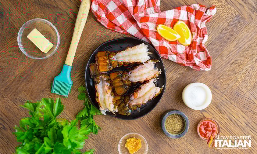 butterflied lobster tails on a black plate surrounded by ingredients