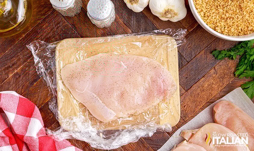 pounded chicken breast on plastic wrap seasoned with salt and pepper