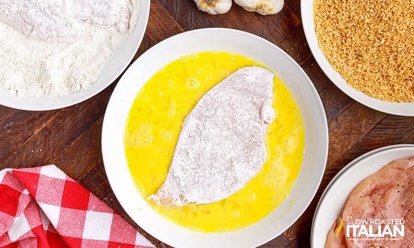 flour-coated chicken cutlet in bowl of whisked eggs