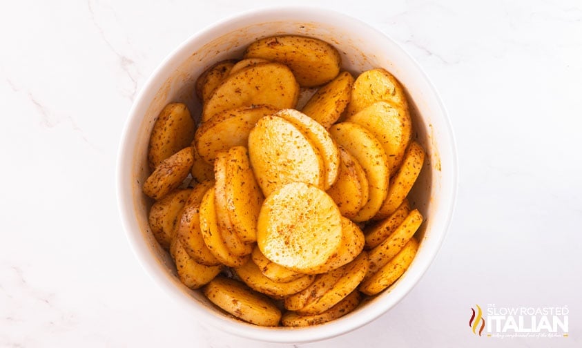 bowl of sliced potatoes coated in oil and spices