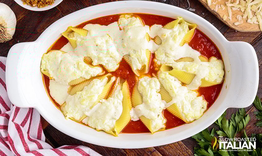 cheese stuffed shells sitting in marinara covered in creamy white sauce