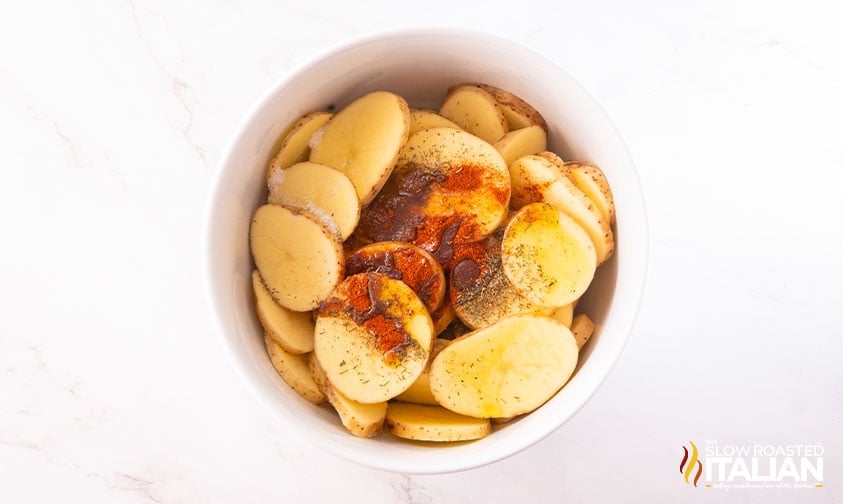bowl of sliced potatoes topped with oil and spices
