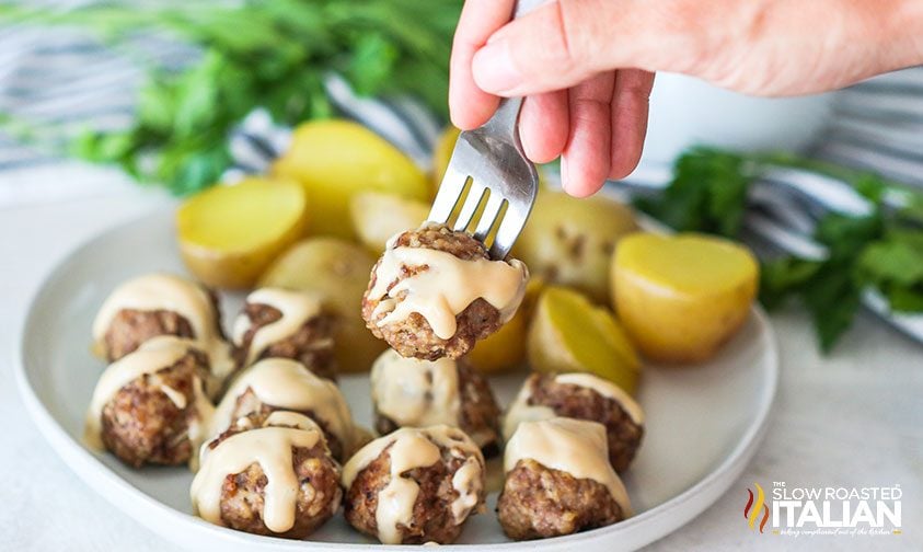 lifting homemade swedish meatball with gravy off plate with a fork