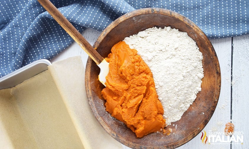 adding pumpkin puree to spice cake mix in wooden bowl