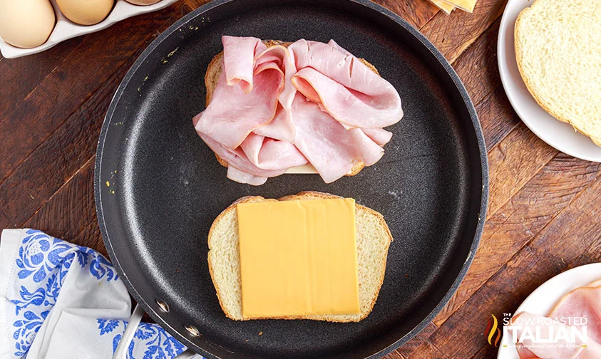 two slices of bread in skillet, one topped with sliced ham and the other with American cheese