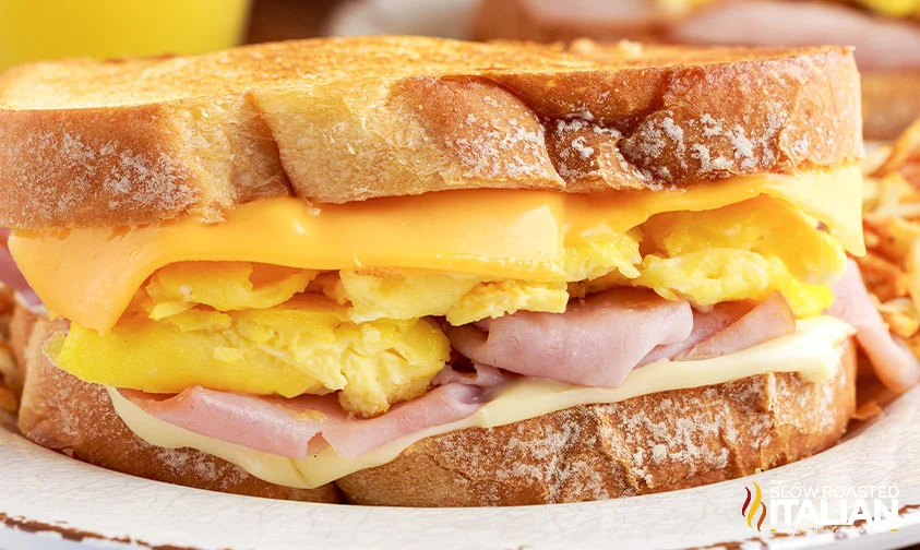 closeup: layers of Swiss cheese, sliced ham, eggs, and American cheese on sandwich