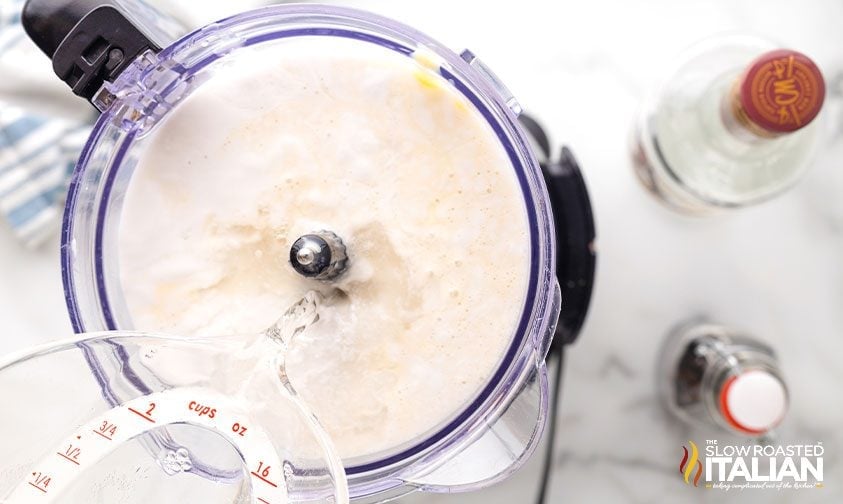 pouring coconut rum into blender with coquito ingredients