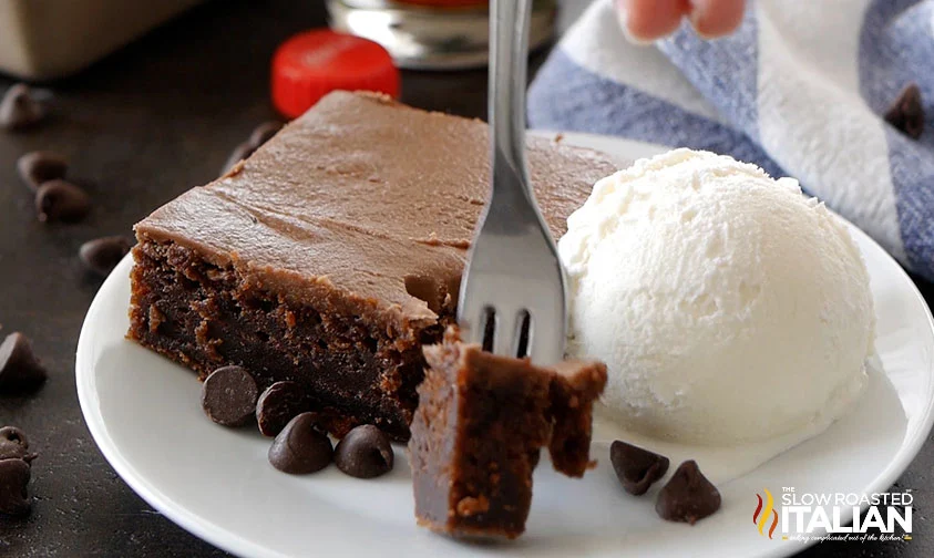 removing forkful of coca cola cake slice, on a plate with chocolate chips and a scoop of vanilla ice cream