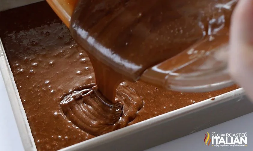 pouring coca cola cake batter into a metal pan