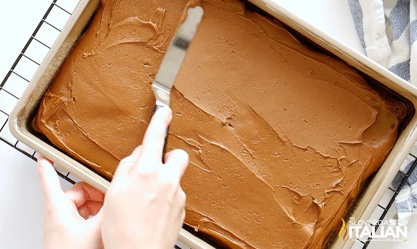 spreading chocolate frosting onto sheet cake with offset spatula