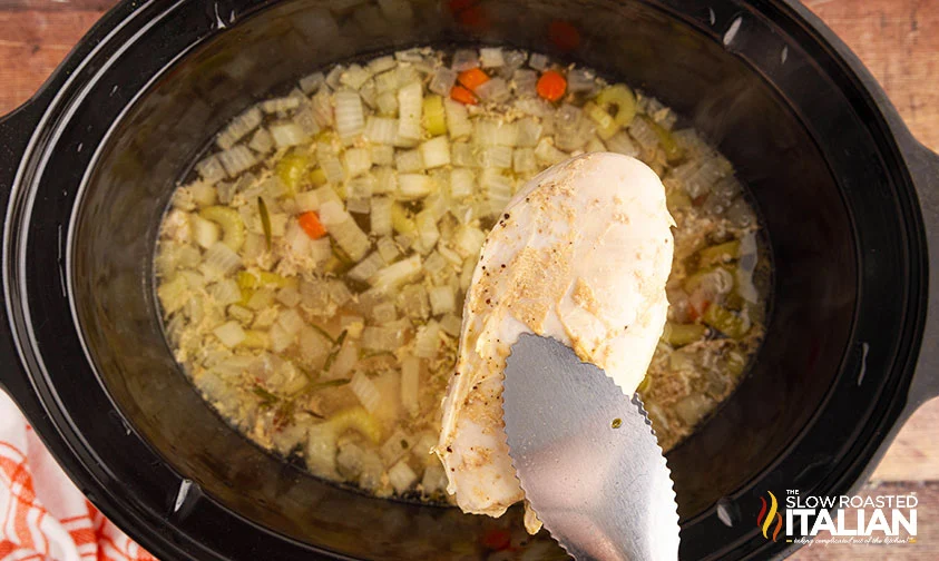 removing cooked chicken breast from crockpot with tongs