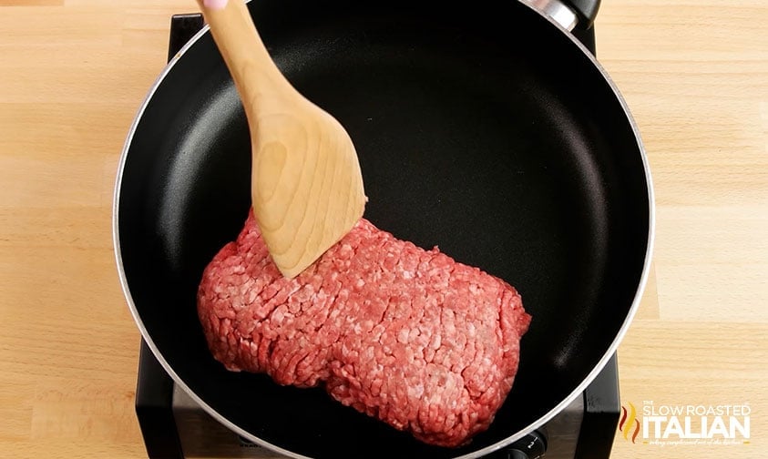 breaking up ground beef in skillet with wooden spatula