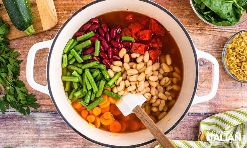 stirring beans and veggies into pot to make minestrone soup like olive garden