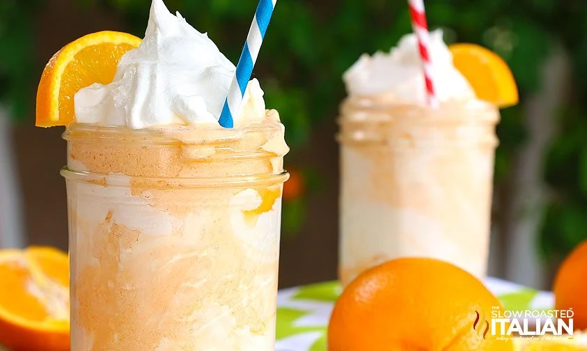 creamsicle orange shakes served in mason jars with whipped cream, orange slice, and striped straw