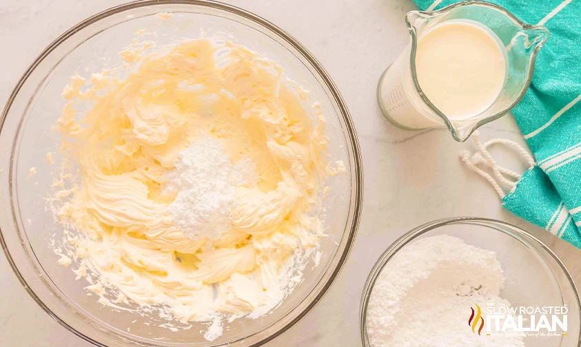 adding powdered sugar and heavy cream to whipped cream cheese