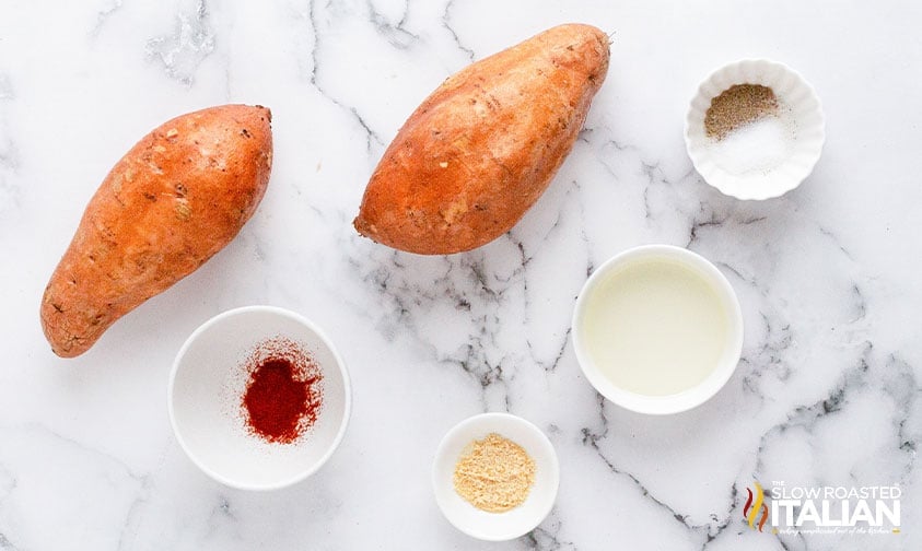 unpeeled sweet potatoes with bowls of oil and seasonings