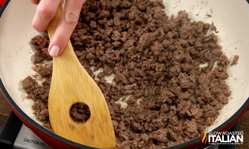 breaking up browned ground beef with a wooden spatula