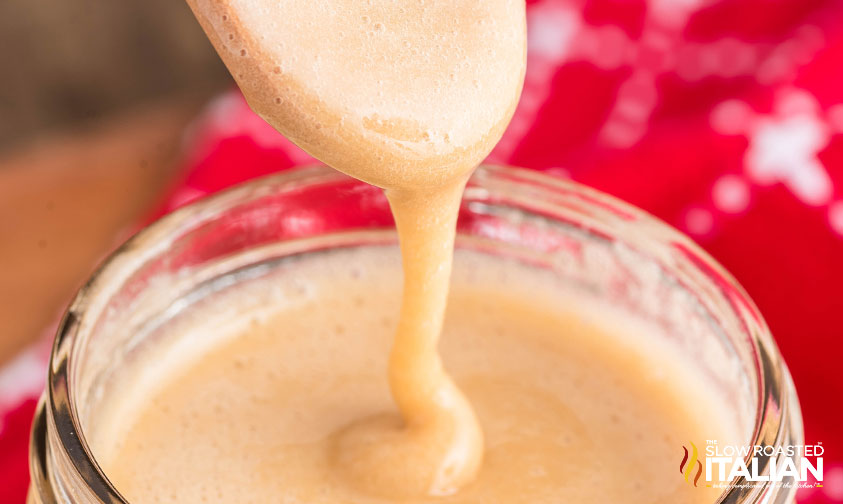 closeup of homemade maple cream drizzled from a spoon into a glass jar