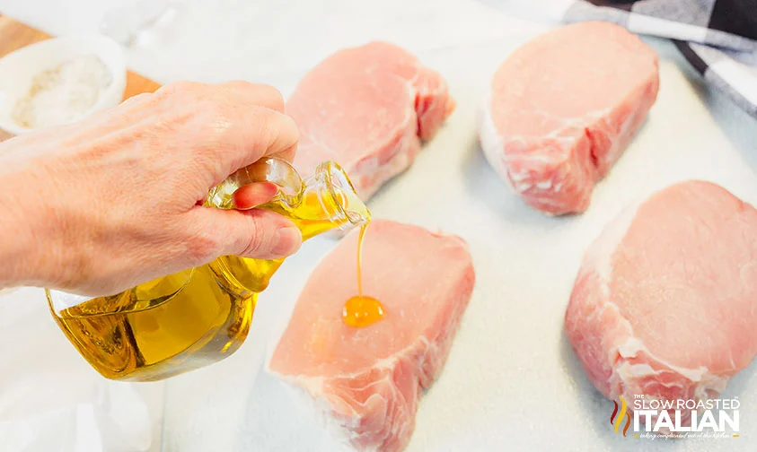 pouring olive oil onto uncooked pork chop