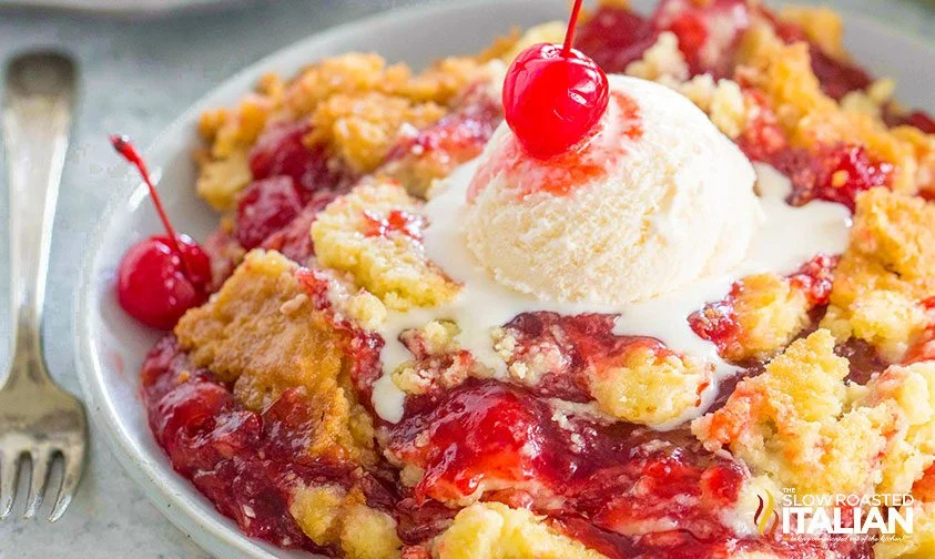 serving of cherry pie filling cake topped with ice cream and maraschino cherry