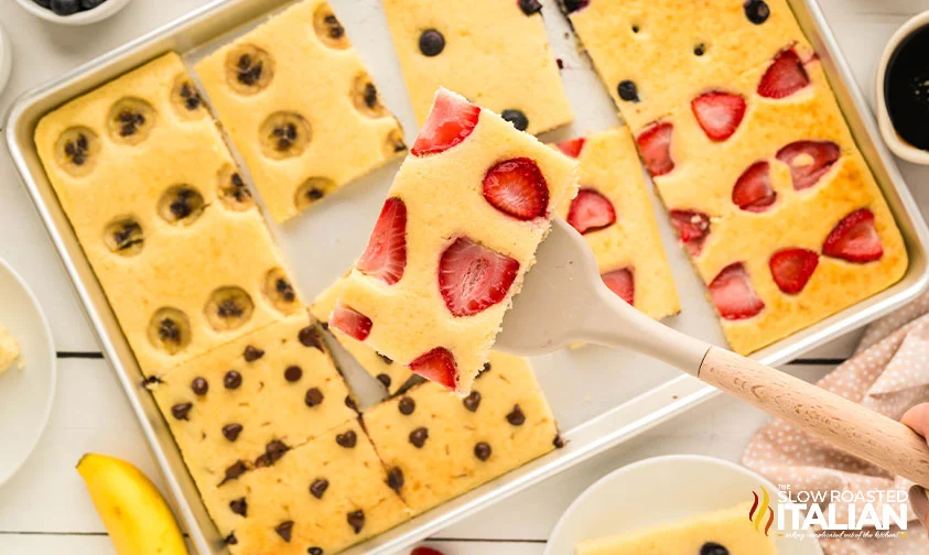 lifting slice of pancake with strawberries from sheet pan
