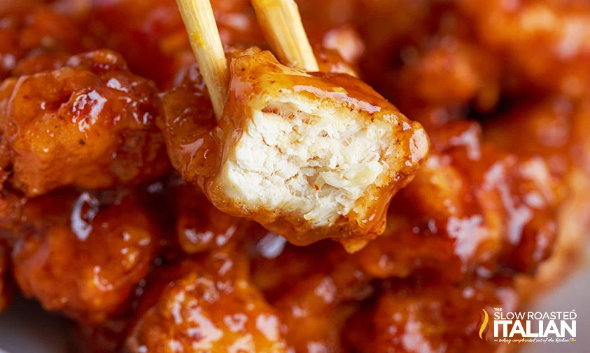 holding piece of orange chicken with chop sticks, showing how juicy it is inside