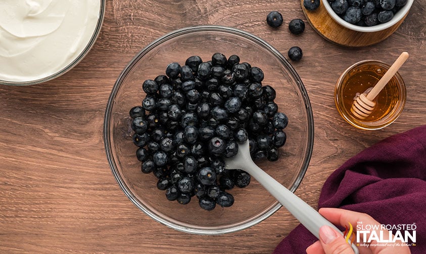 mixing fresh blueberries with honey in a glass bowl