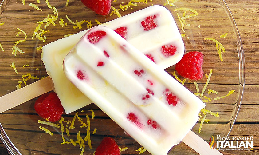 closeup of two lemon raspberry popsicles with lemon zest and fresh raspberries