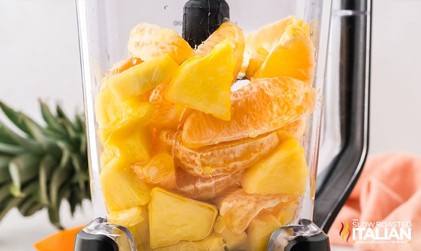 pieces of orange and chunks of pineapple in a blender