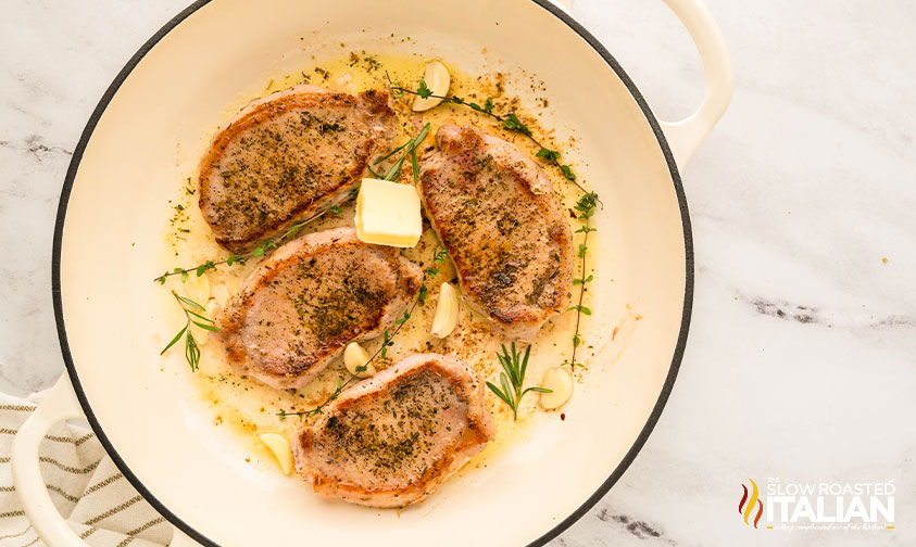 adding butter, garlic cloves, and rosemary sprigs in large skillet