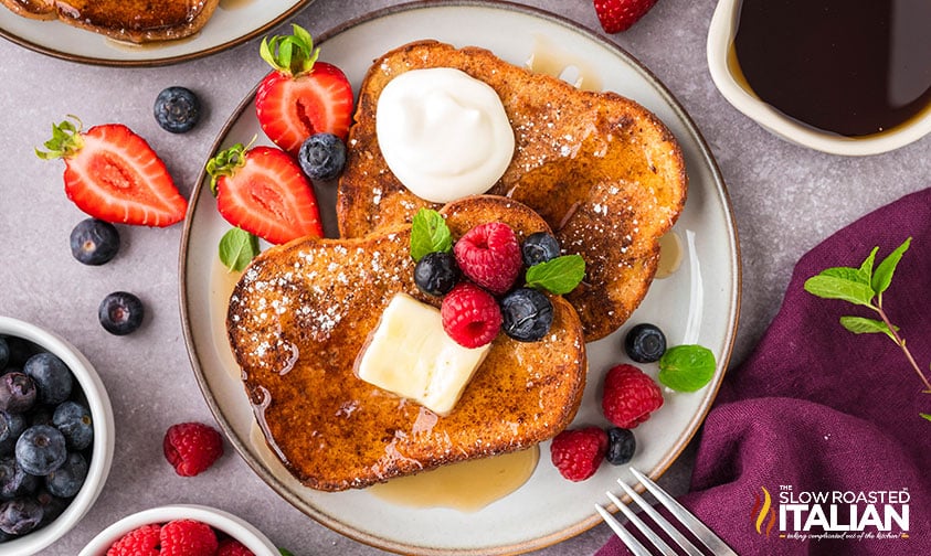 sheet pan french toast on a plate with butter, syrup, and berries