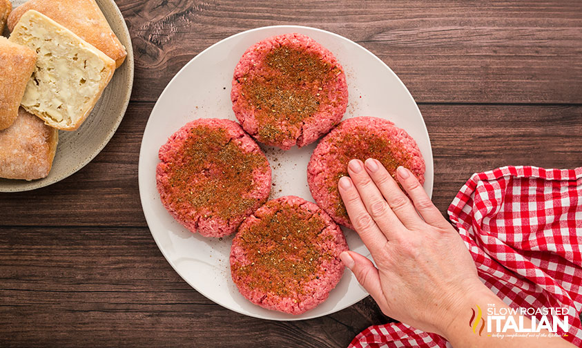 adding seasoning to burger patties on a plate