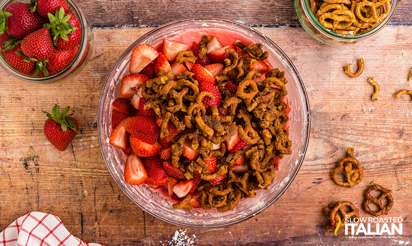 adding strawberries and pretzels to strawberry cheesecake salad