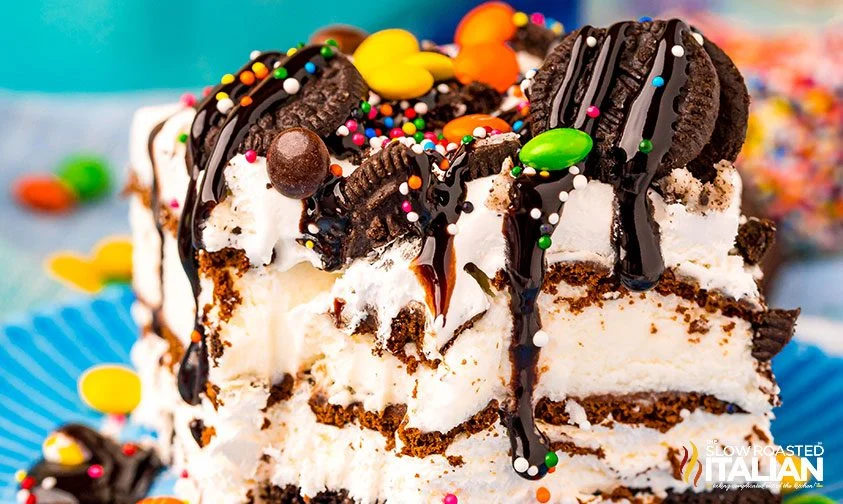 closeup: slice of oreo and ice cream sandwich cake topped with candies and chocolate syrup
