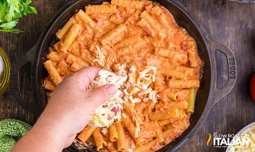 sprinkling shredded cheese over ziti pasta with sauce