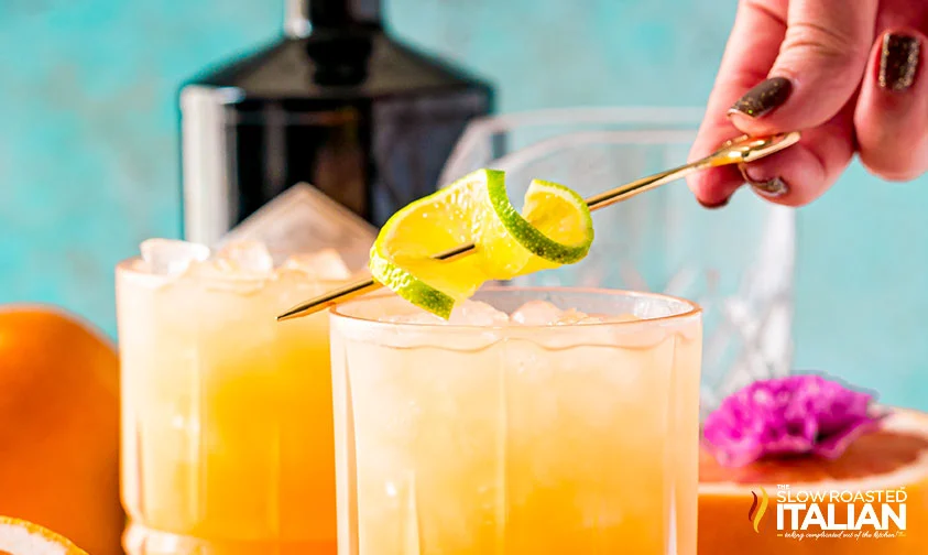 placing cocktail skewer with twisted lime slice onto rim of greyhound drink