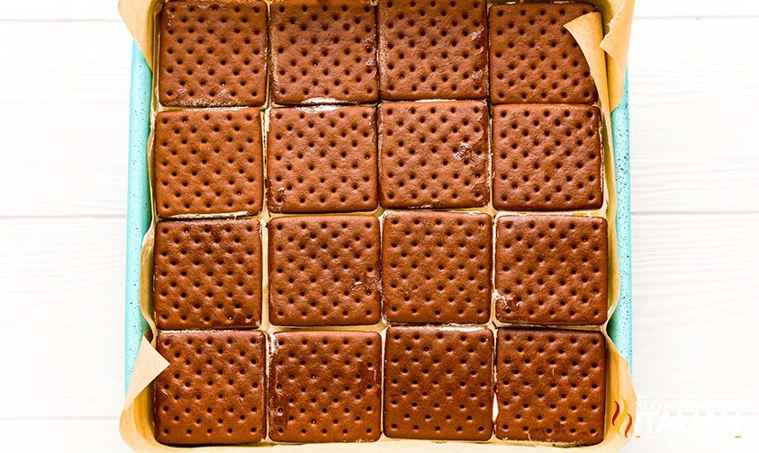 a layer of square ice cream sandwiches in a parchment-lined pan