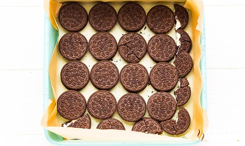 Oreo cookies, some broken in half, covering the bottom of a parchment-lined baking sheet