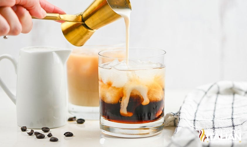 adding creamer to glass of vodka and kahlua with ice