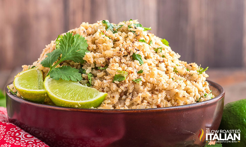 side view: chipotle cauliflower rice in a bowl with lime wedges and cilantro