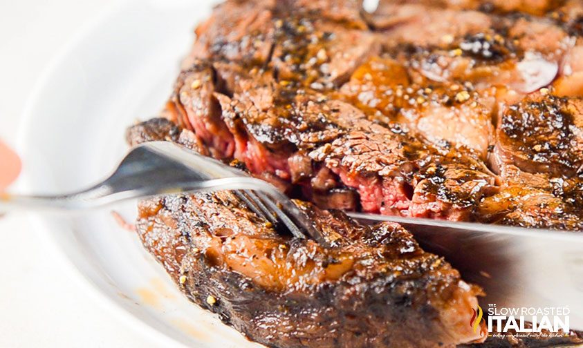 closeup: cutting grilled ribeye steak with a fork and knife