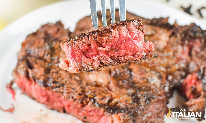 closeup: a fork holding a piece of grilled ribeye steak